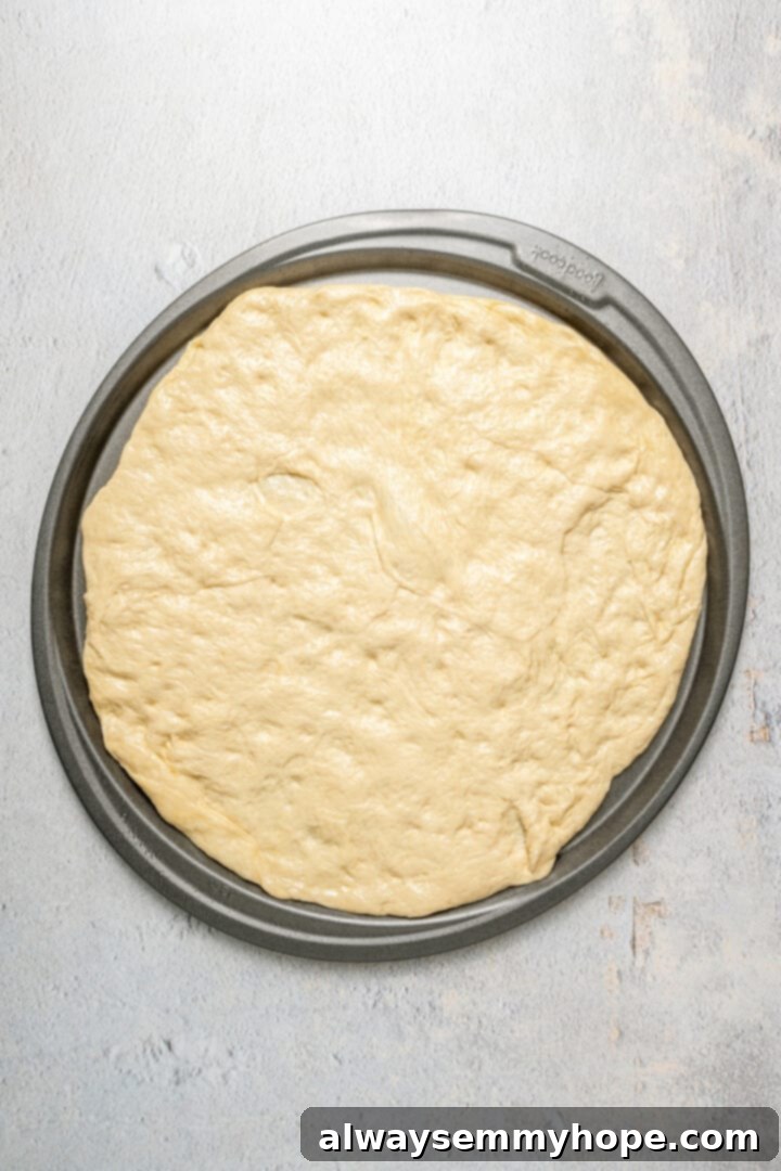 This vegan breakfast pizza features plant-based eggs, cheese, hash browns, and sausage, all baked on a crispy, chewy crust. So good! A smooth, round pizza crust rests on a pizza pan, perfectly shaped and ready for toppings.