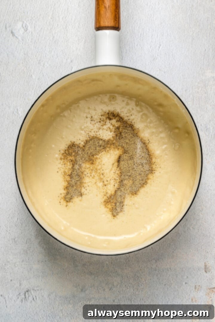 This vegan breakfast pizza features plant-based eggs, cheese, hash browns, and sausage, all baked on a crispy, chewy crust. So good! A creamy, off-white vegan breakfast gravy in a small saucepan, after seasonings have been added, showing a smooth and rich texture.