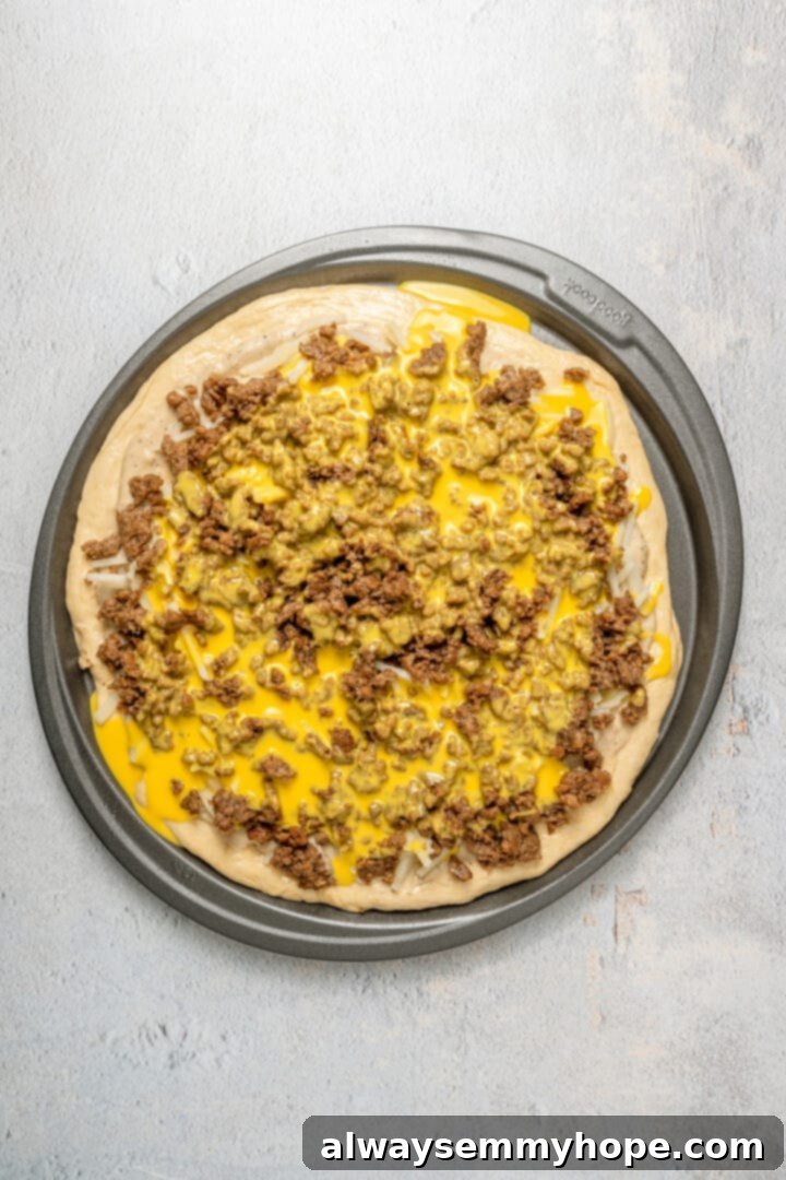 This vegan breakfast pizza features plant-based eggs, cheese, hash browns, and sausage, all baked on a crispy, chewy crust. So good! An unbaked vegan breakfast pizza, now fully loaded with plant-based egg batter poured over the toppings, before adding the final layer of cheese.
