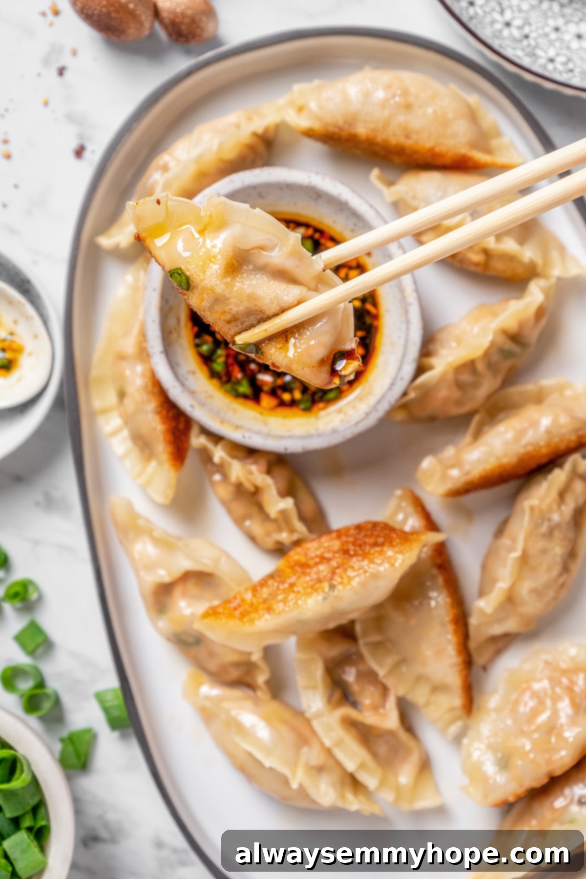 Overhead view of dumpling being held over dipping sauce with chopsticks