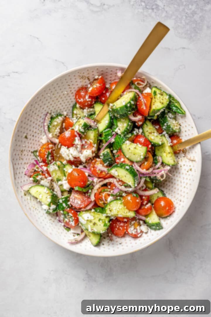 Crisp cucumbers and sun-ripened tomatoes are tossed in a simple vinaigrette for a refreshing, flavourful vegan cucumber and tomato salad. Overhead view of a finished vegan cucumber and tomato salad, beautifully arranged in a serving bowl with two gold serving spoons.