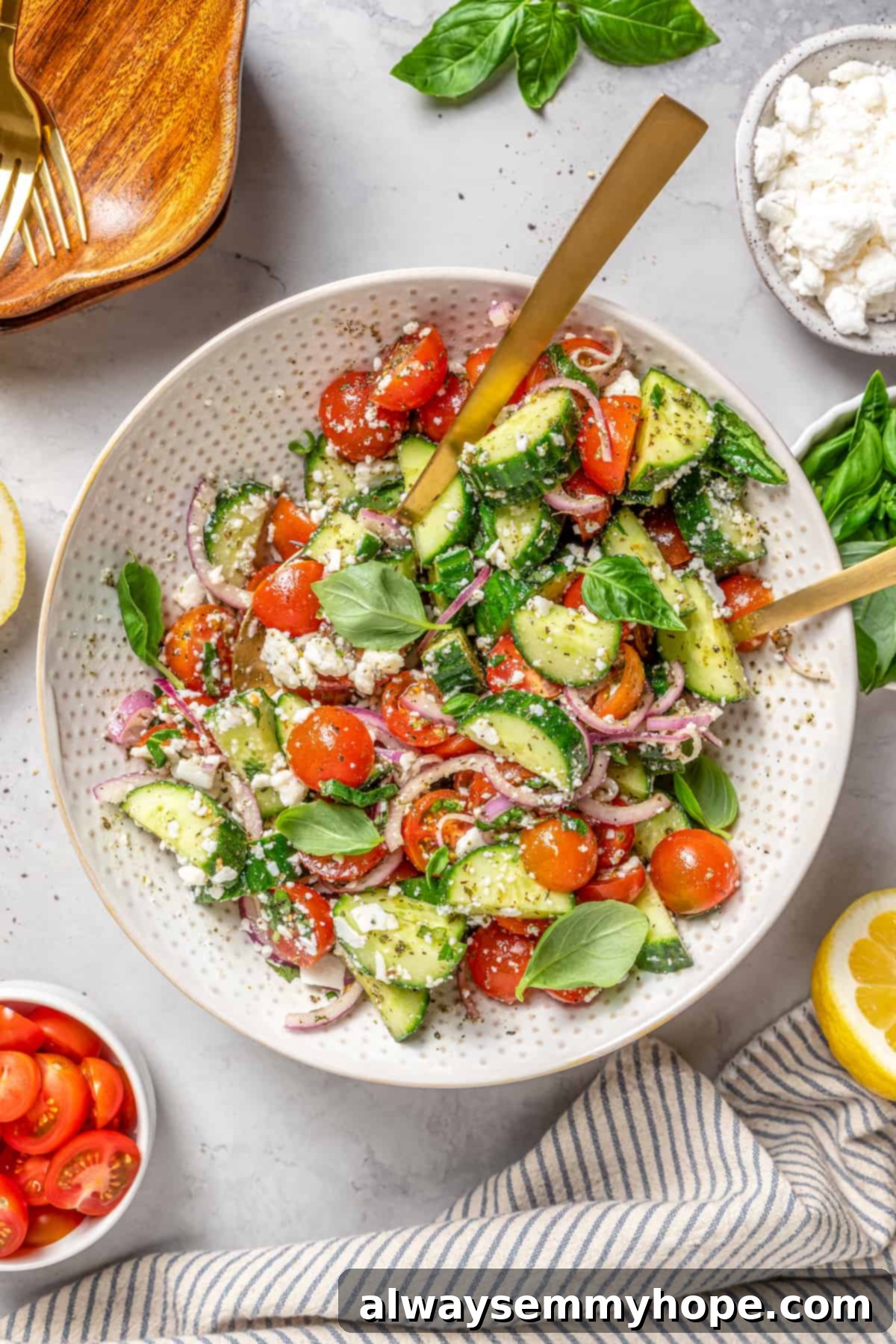 Crisp cucumbers and sun-ripened tomatoes are tossed in a simple vinaigrette for a refreshing, flavourful vegan cucumber and tomato salad. Overhead view of a beautiful vegan cucumber and tomato salad served in a rustic bowl, accompanied by two elegant gold serving spoons.