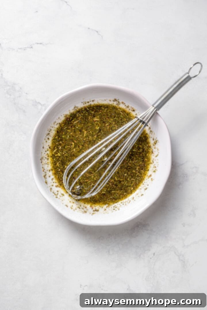 Crisp cucumbers and sun-ripened tomatoes are tossed in a simple vinaigrette for a refreshing, flavourful vegan cucumber and tomato salad. Overhead view of a small bowl containing the freshly whisked herbed vinaigrette, with a small whisk resting inside.
