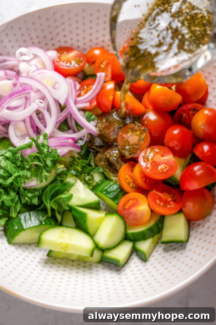Crisp cucumbers and sun-ripened tomatoes are tossed in a simple vinaigrette for a refreshing, flavourful vegan cucumber and tomato salad. Close-up shot of a stream of vinaigrette being poured from a bowl into a larger bowl of mixed vegetables for the cucumber and tomato salad.