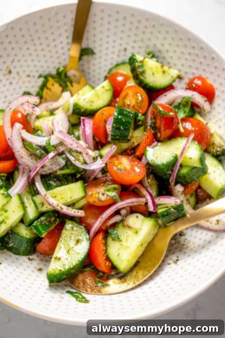 Crisp cucumbers and sun-ripened tomatoes are tossed in a simple vinaigrette for a refreshing, flavourful vegan cucumber and tomato salad. Overhead view of a serving bowl filled with a tossed vegan cucumber and tomato salad, featuring two gold serving spoons nestled within.