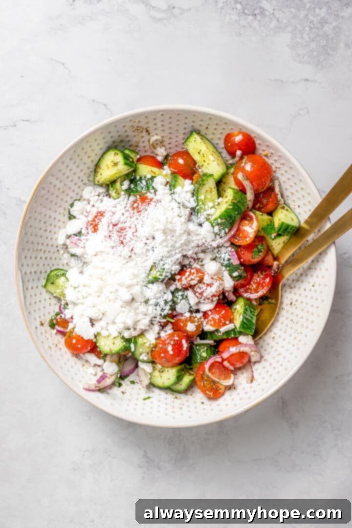 Crisp cucumbers and sun-ripened tomatoes are tossed in a simple vinaigrette for a refreshing, flavourful vegan cucumber and tomato salad. Overhead view of crumbled vegan feta being added generously to the vibrant cucumber and tomato salad in a bowl.