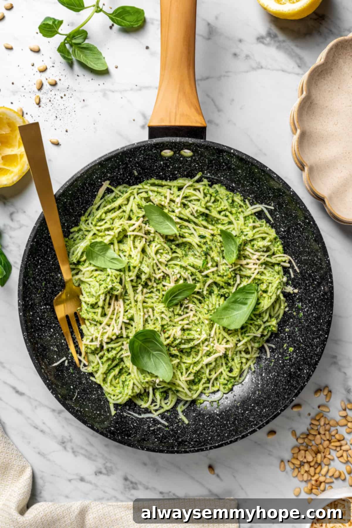 Overhead view of hearts of palm pesto pasta in skillet with basil leaves for garnish and gold fork