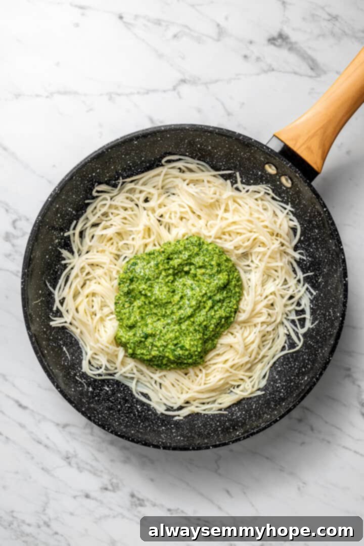 Overhead view of pesto added to skillet of hearts of palm pasta