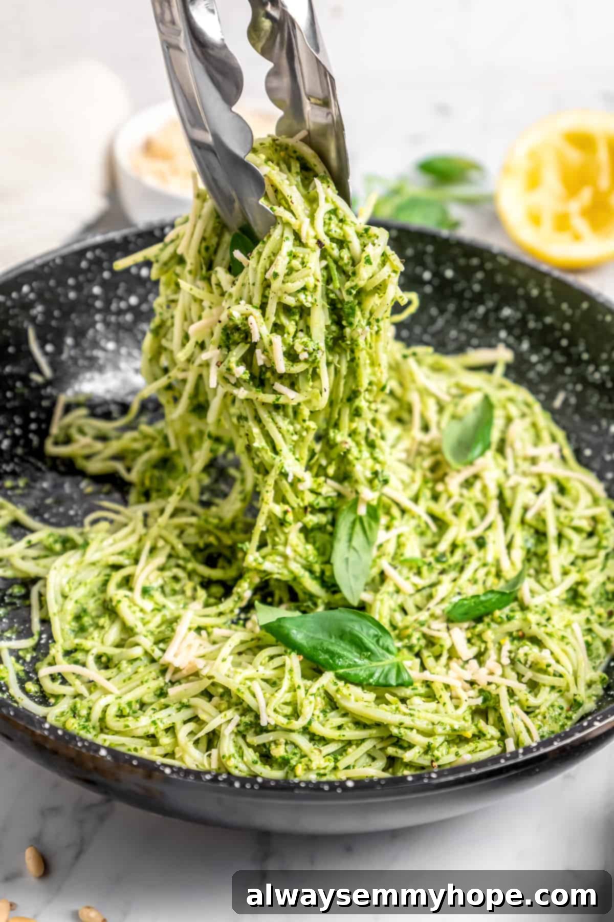 Tongs tossing hearts of palm pasta with pesto in skillet