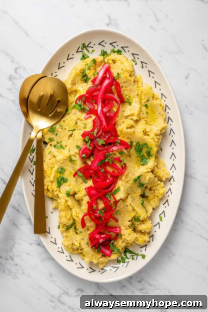 Overhead view of beautifully presented vegan mangú on a platter, garnished with fresh cilantro and pickled red onions, with two serving spoons.
