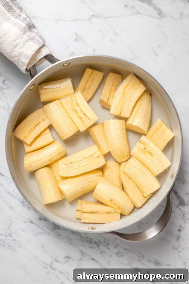 Overhead view of raw, peeled green plantain pieces placed in a large pot, ready to be covered with water and cooked.