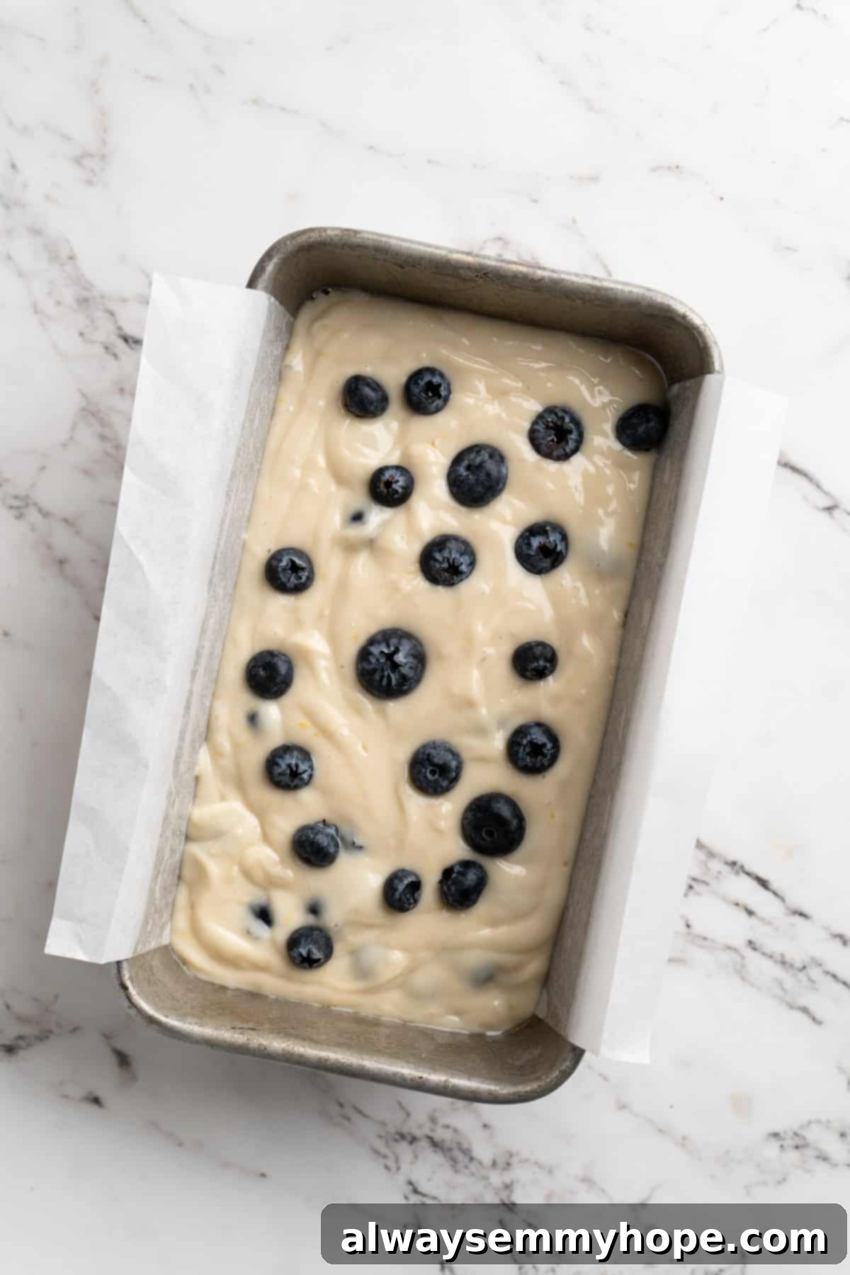 Overhead view of lemon blueberry bread batter in a loaf pan, topped with extra blueberries, ready to bake.