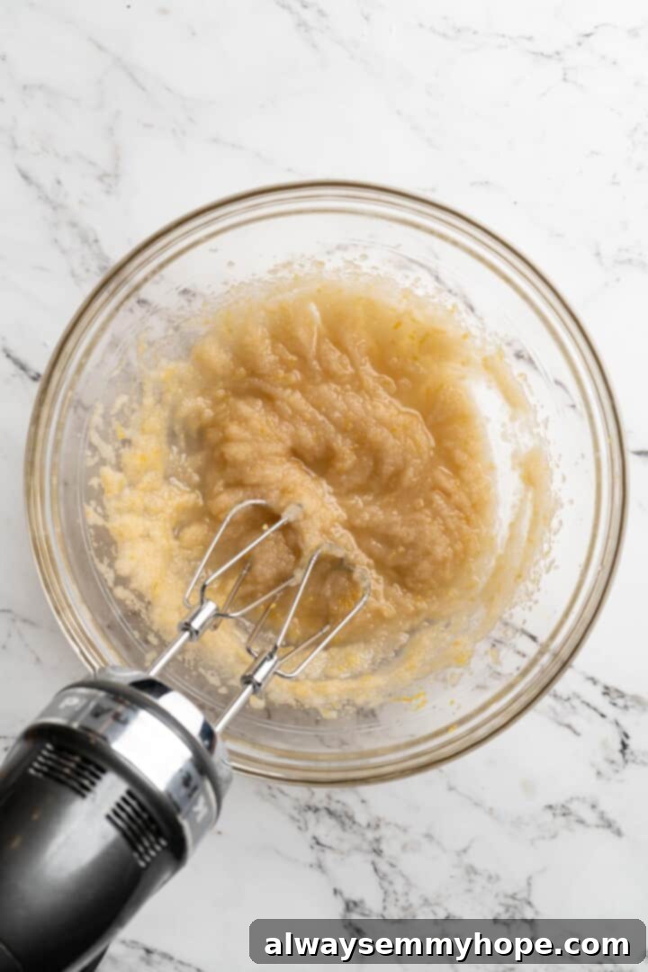 Overhead view of a stand mixer creaming cane sugar and oil in a large mixing bowl.