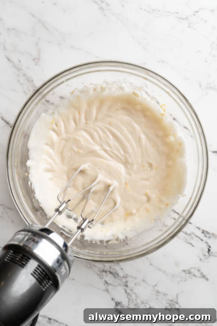 Overhead view of a mixer beating wet ingredients for quick bread batter, including extracts and lemon zest.
