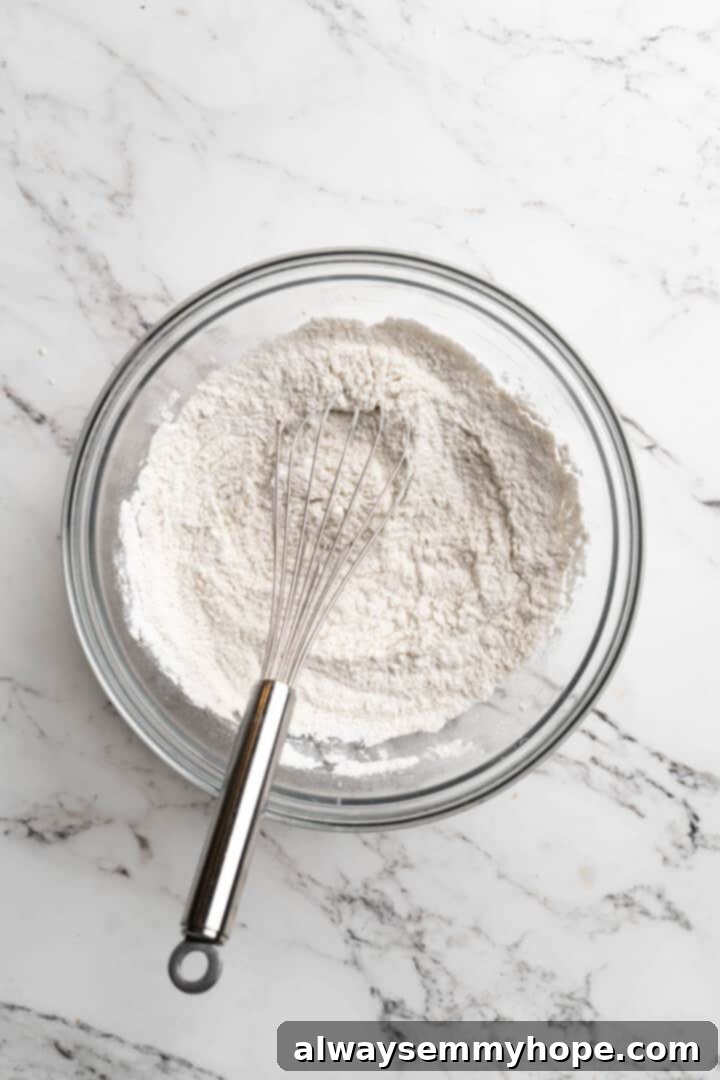 Overhead view of dry ingredients for quick bread, including flour, baking powder, baking soda, and sea salt, in a glass bowl with a whisk.