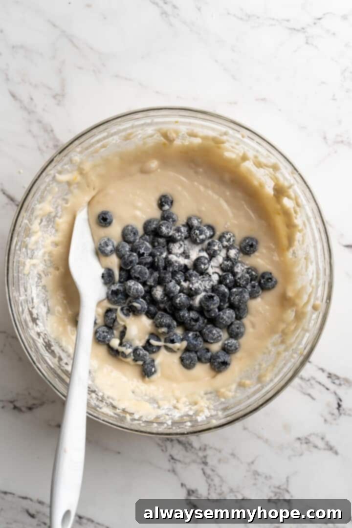 Overhead view of flour-dusted blueberries gently folded into the lemon bread batter in a glass bowl.