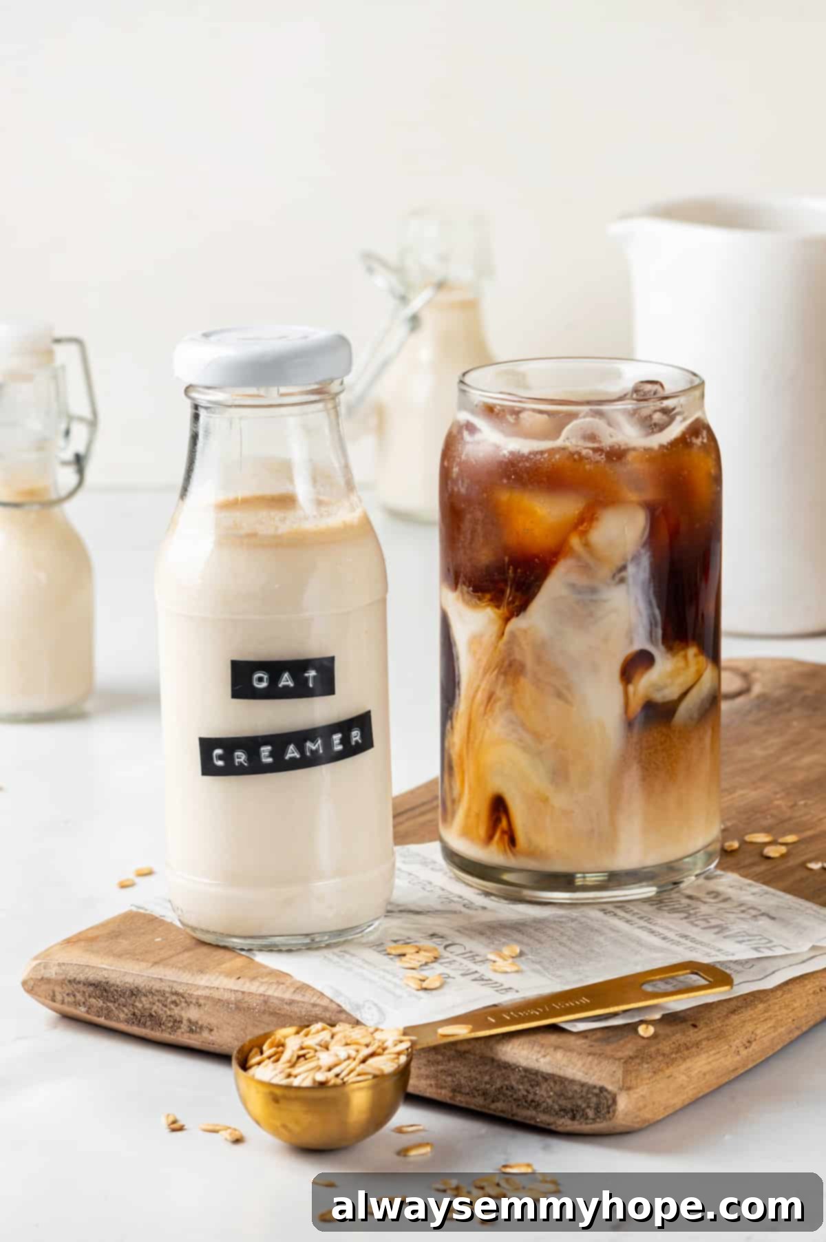 A bottle of homemade oat milk coffee creamer next to a refreshing glass of iced coffee on a rustic cutting board.