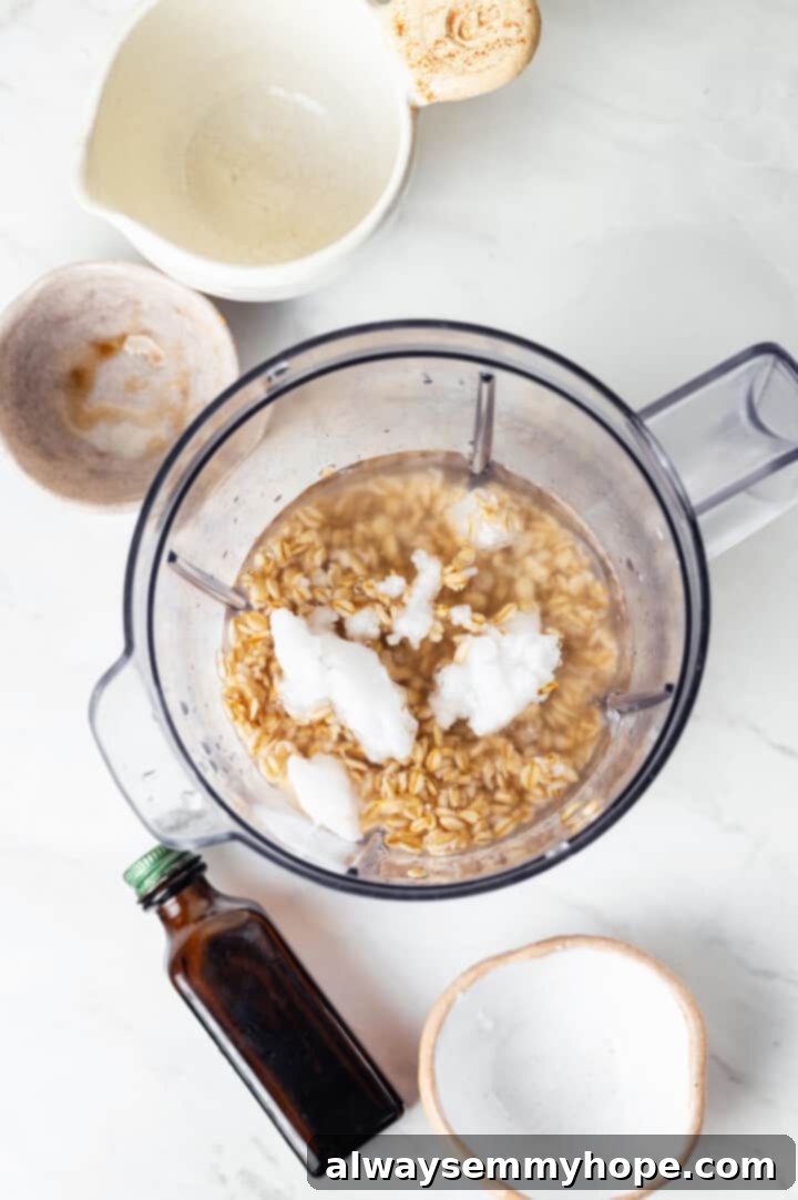 Overhead view of all ingredients for oat milk coffee creamer, including drained oats, in a blender jar, ready to be processed.