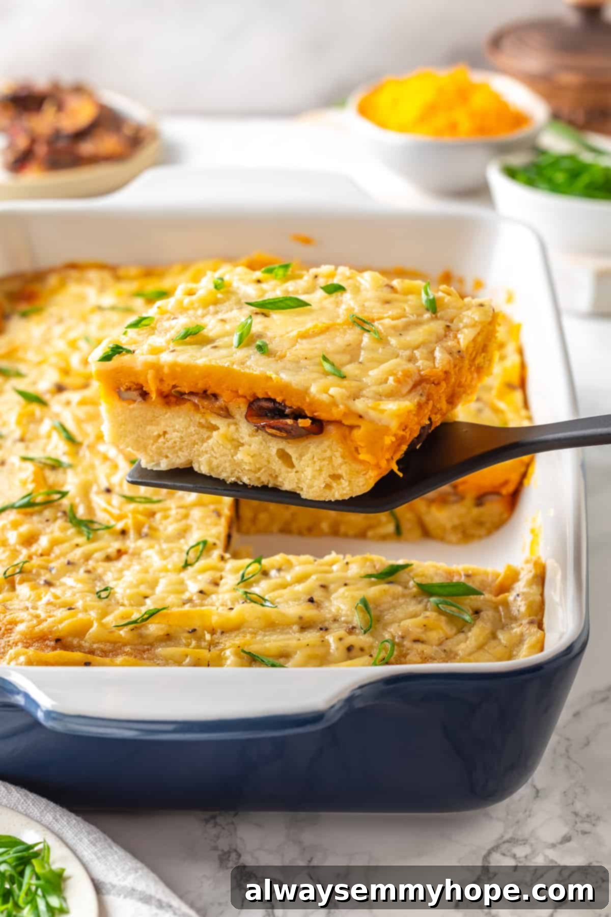 Love biscuits and gravy? You’re going to flip for biscuits and gravy casserole! The comfort food you love in a crowd-pleasing casserole. Spatula lifting a generous portion of vegan biscuits and gravy casserole from a baking dish, showing off the layers of biscuit, mushrooms, cheese, and gravy