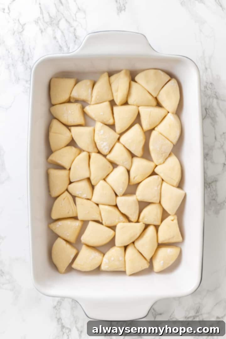 Love biscuits and gravy? You’re going to flip for biscuits and gravy casserole! The comfort food you love in a crowd-pleasing casserole. Overhead view of biscuit dough pieces uniformly arranged in a casserole dish, forming the base layer