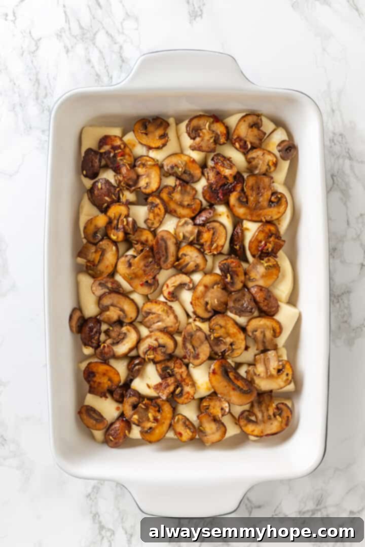 Love biscuits and gravy? You’re going to flip for biscuits and gravy casserole! The comfort food you love in a crowd-pleasing casserole. Overhead view of the sautéed mushroom layer evenly spread over the biscuit pieces in the casserole dish