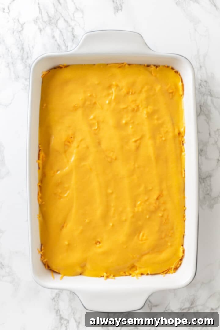 Love biscuits and gravy? You’re going to flip for biscuits and gravy casserole! The comfort food you love in a crowd-pleasing casserole. Overhead view of the vegan egg batter being poured evenly over the cheese and mushroom layers in the casserole dish
