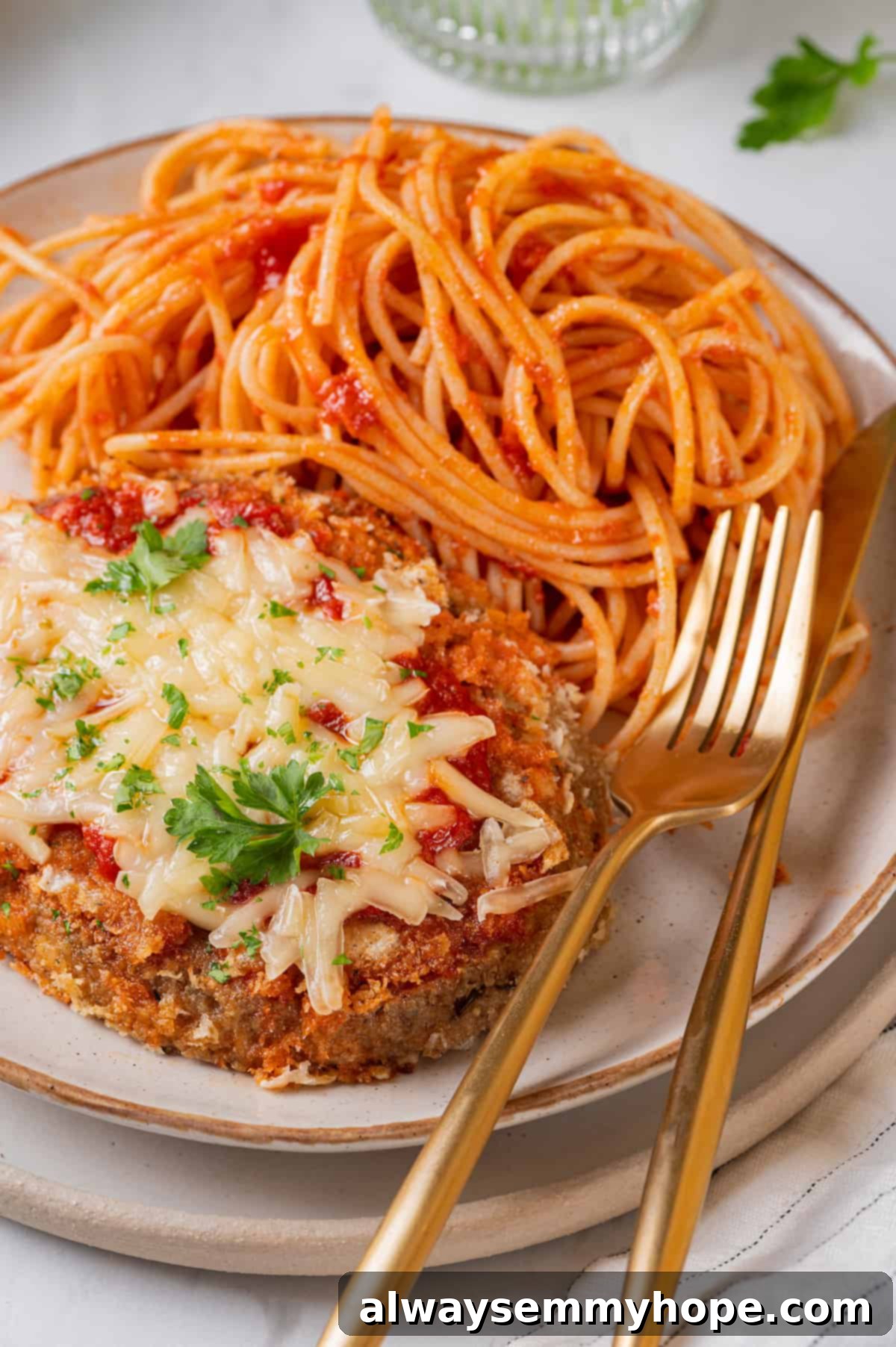 Plate with spaghetti and chicken parmesan, with gold knife and fork set to the side