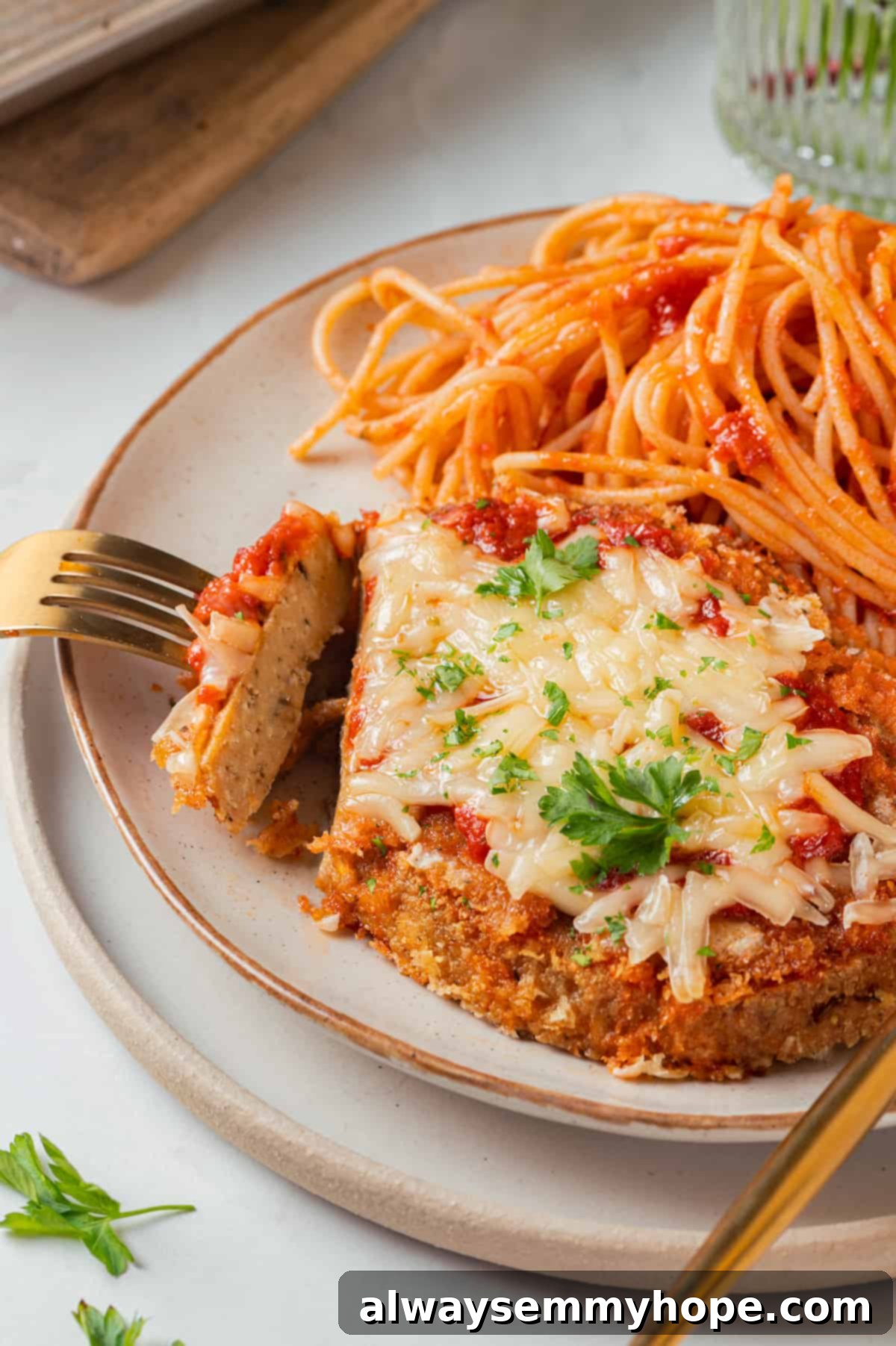 Fork pulling away slice of chicken parmesan on plate with spaghetti