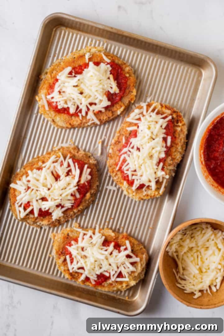 Overhead view of chicken parmesan cutlets on baking sheet after adding sauce and vegan cheese