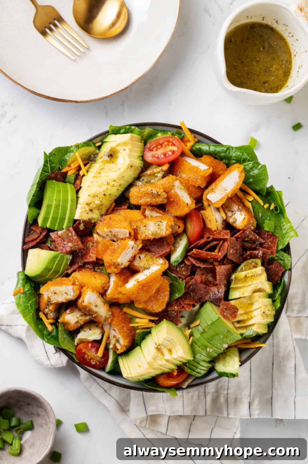 An inviting overhead view of a fully assembled vegan Chick-fil-A Cobb salad in a large bowl, showcasing colorful layers of plant-based chicken, avocado, tomatoes, green onions, and shredded carrots.