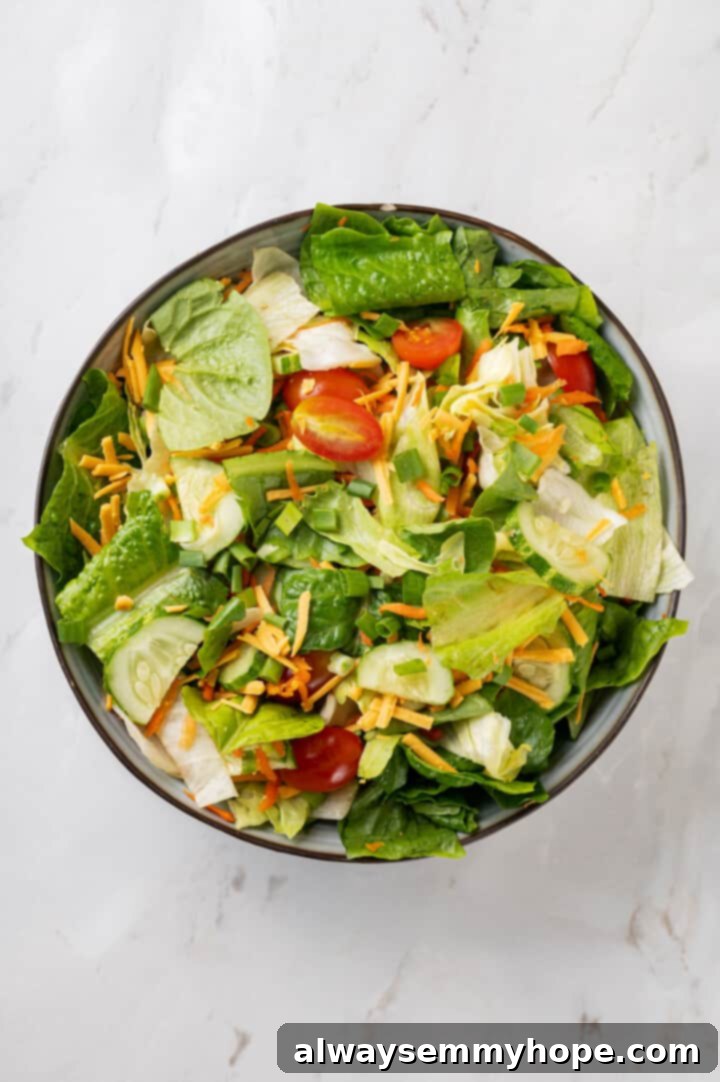 Overhead shot of the base of the copycat Chick-Fil-A Cobb salad, showing a generous amount of mixed greens, green onions, and other vegetables in a large bowl, ready for protein and dressing.