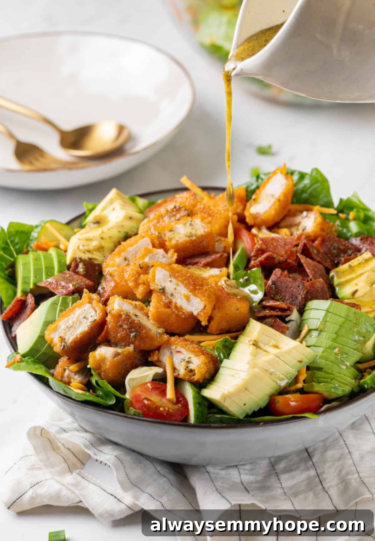 A hand pouring homemade dressing over a vibrant vegan Chick-fil-A Cobb salad, highlighting the fresh ingredients and the rich vinaigrette.