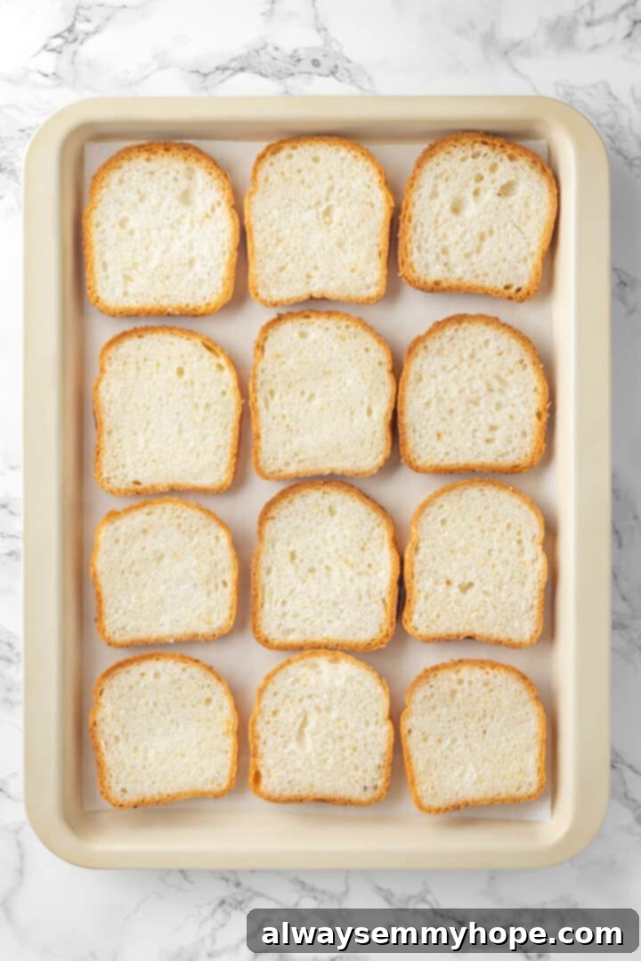 Overhead view of unbuttered bread slices neatly arranged on a parchment-lined sheet pan.