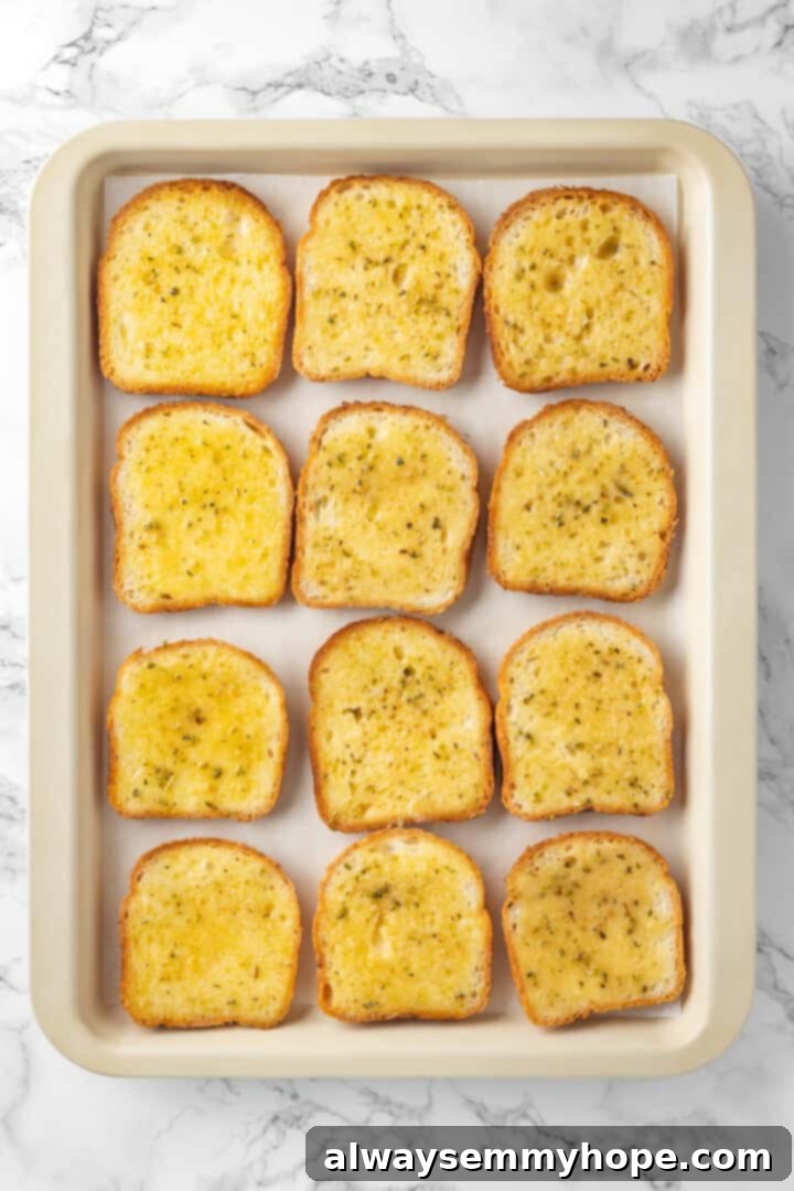 Overhead view of Texas toast slices on a sheet pan, with one side generously brushed with garlic butter.