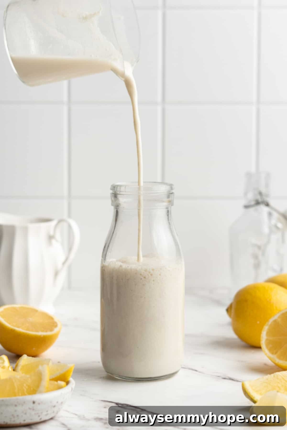 Achieve perfect dairy-free buttermilk with just two ingredients. Essential for vegan baking! Pouring homemade vegan buttermilk from a liquid measuring cup into a clear glass bottle, showcasing its creamy consistency.