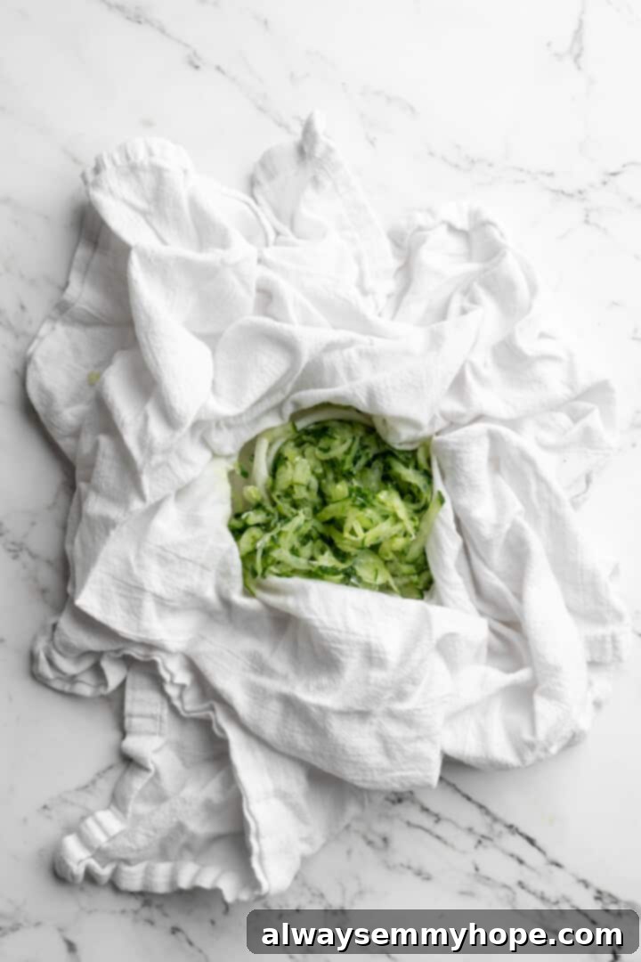 Homemade vegan tzatziki is a tangy, refreshing, and garlicky dip with bright lemon flavor. This easy plant-based recipe is perfect for any meal! An overhead view of finely grated cucumber neatly piled in the center of a clean white kitchen towel, ready for straining.