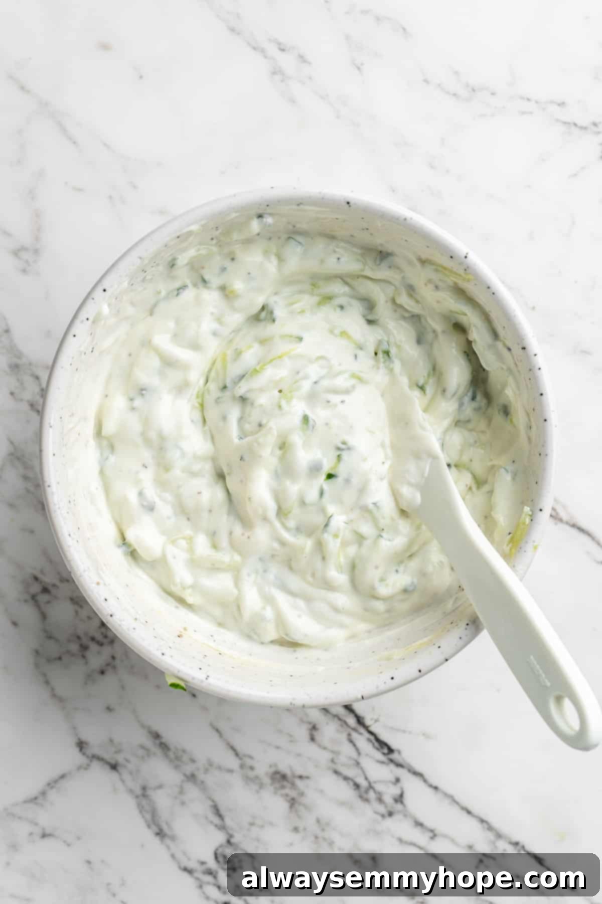 Homemade vegan tzatziki is a tangy, refreshing, and garlicky dip with bright lemon flavour. This easy plant-based recipe is perfect for any meal! An overhead shot of a bowl of creamy vegan tzatziki, perfectly mixed and ready to serve, with a spoon resting in it.