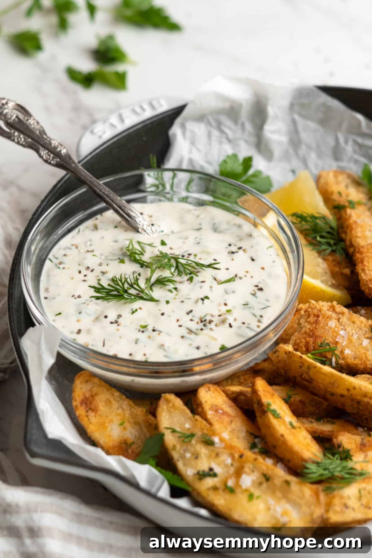 Bowl of tartar sauce garnished with fresh dill on plate of fish and chips