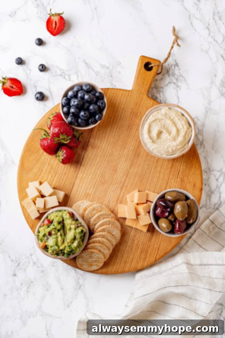 Overhead view of small bowls, vegan cheese, crackers, and strawberries beginning to be arranged on a large round wooden board.