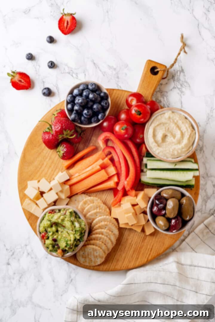 Overhead view of bowls and larger ingredients, like vegan cheese and fruit, already placed on a round wooden board, with space remaining to fill.
