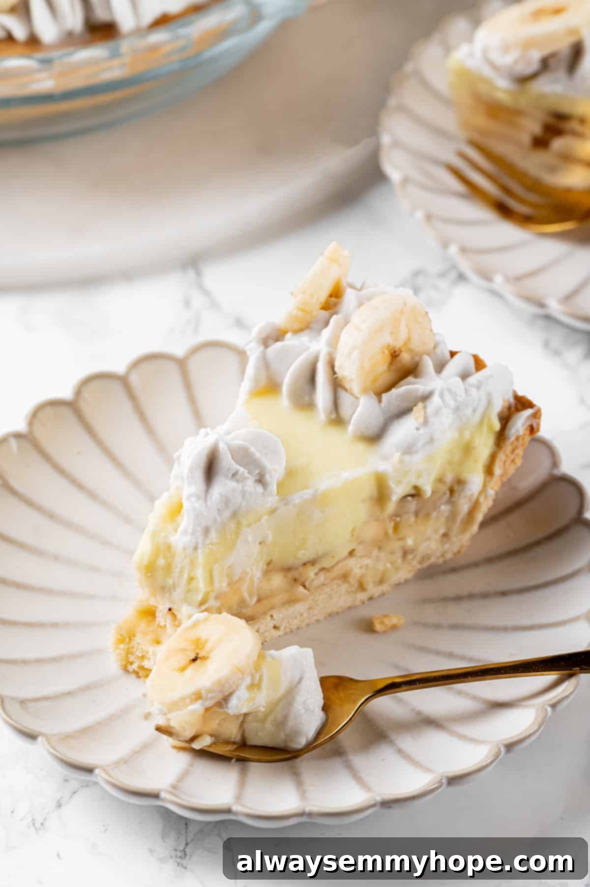 A beautiful slice of vegan banana cream pie on a white plate with a fork, showing off its creamy layers and golden crust.