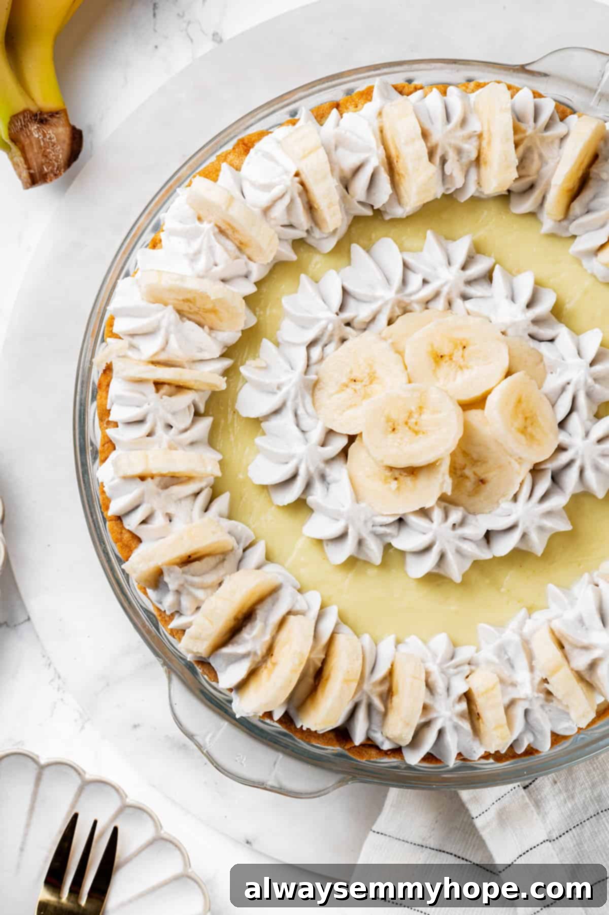 Overhead view of a whole, beautifully decorated vegan banana cream pie, ready to be sliced.