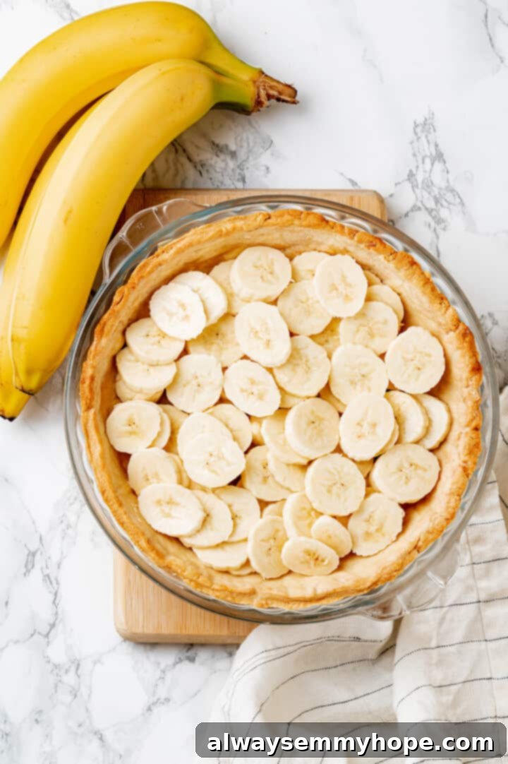 Overhead view of perfectly sliced bananas arranged neatly in a pre-baked vegan pie crust, ready for the filling.