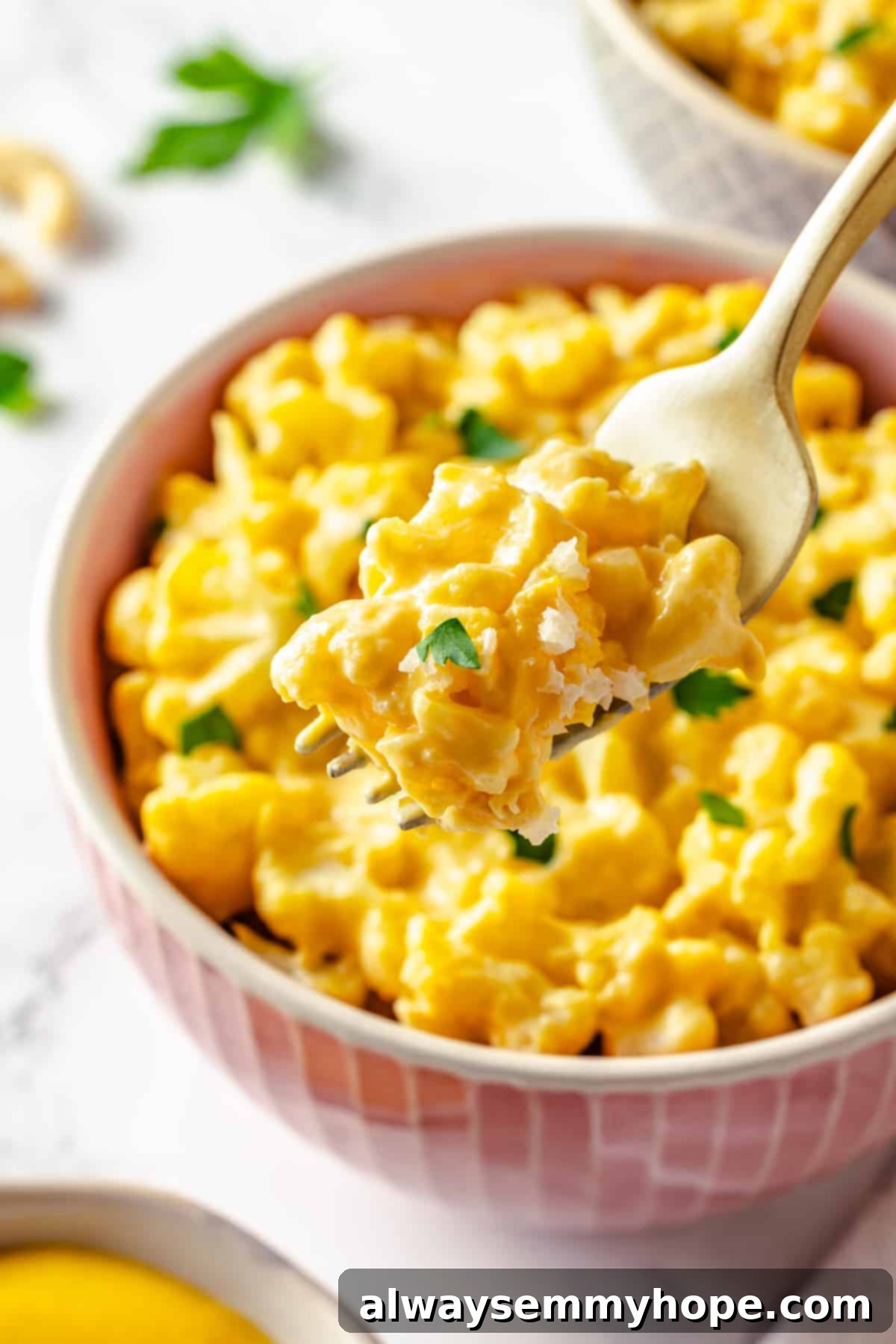 Fork of creamy vegan cauliflower mac and cheese held over a bowl, showcasing its rich texture.