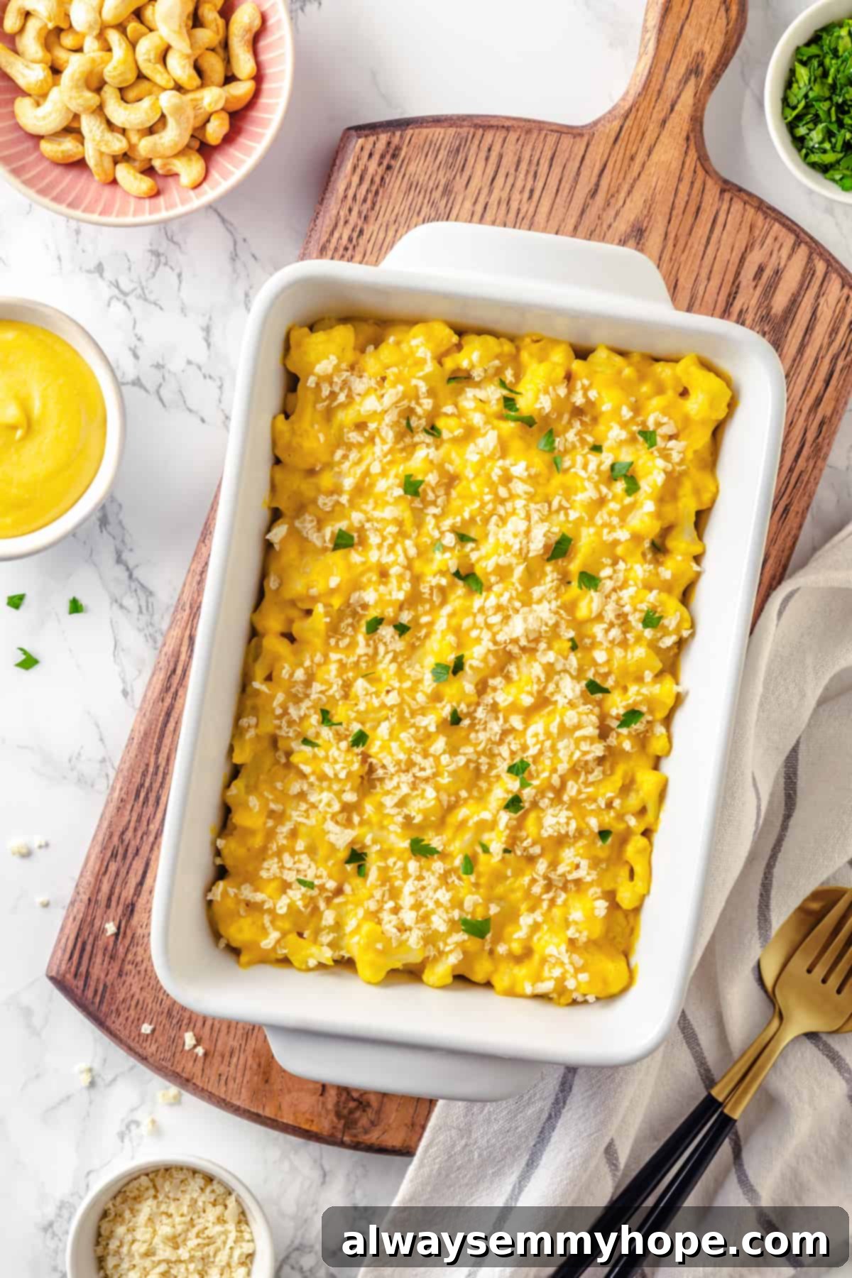 Overhead view of a white baking dish filled with golden-brown vegan cauliflower mac and cheese, presented on a wooden board.