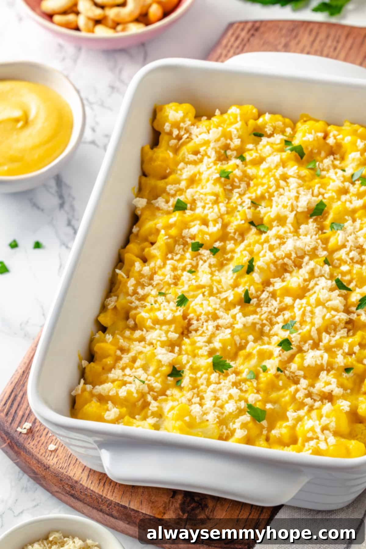 A pristine white baking dish filled with golden-brown vegan cauliflower mac and cheese, ready to be served on a wooden board.