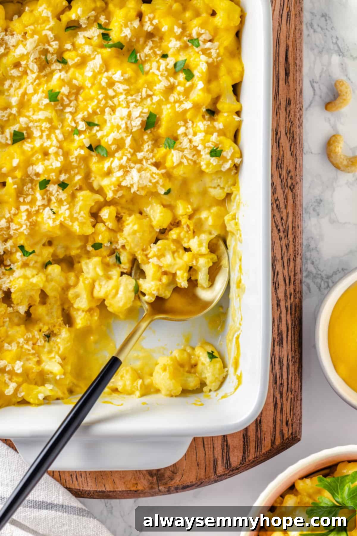 Overhead view of creamy vegan cauliflower mac and cheese in a baking dish, with a serving spoon resting inside.