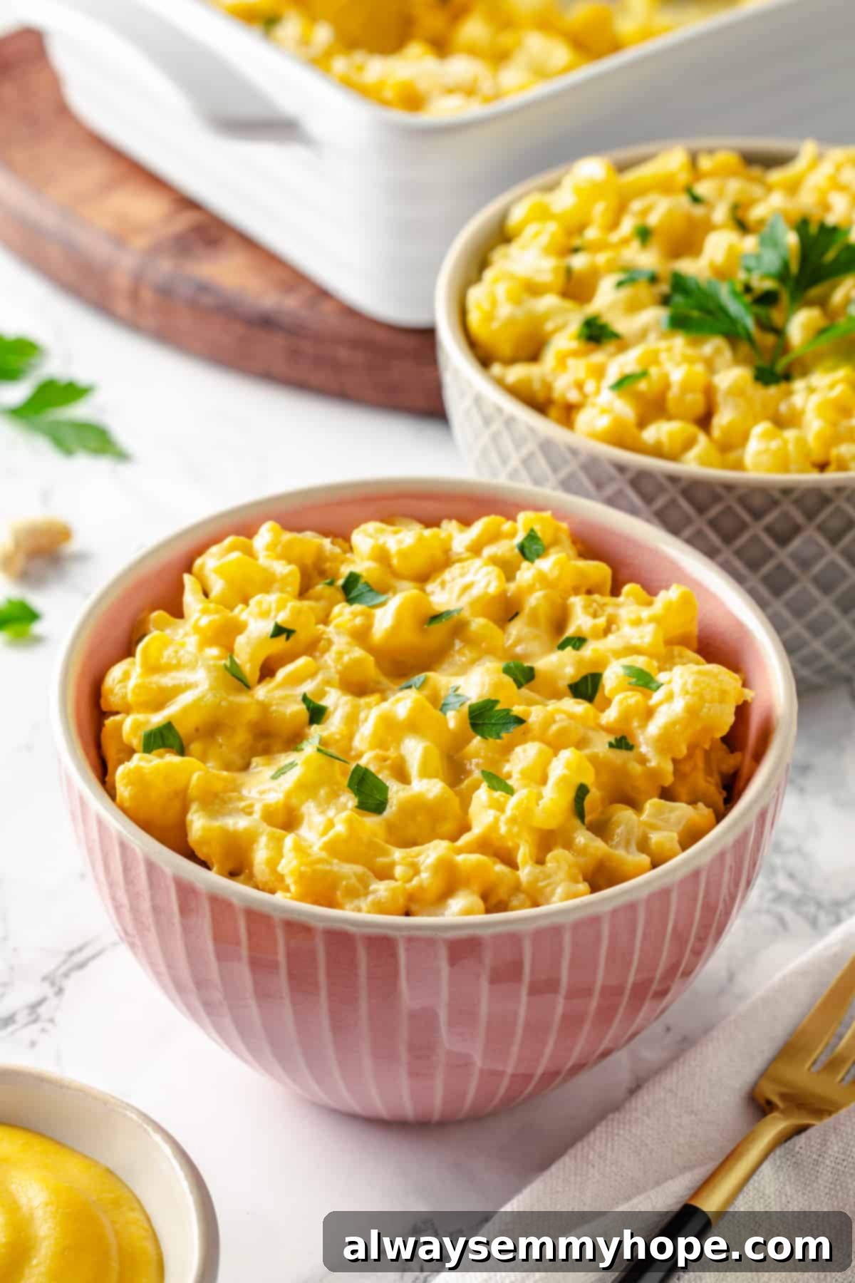 Two bowls of vegan cauliflower mac and cheese in the foreground, with a baking dish of the same dish blurred in the background.