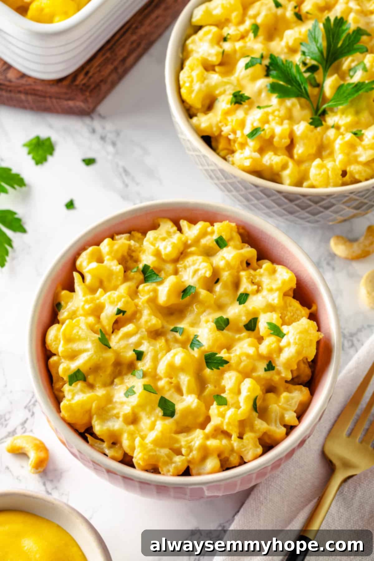 Two bowls of vegan cauliflower mac and cheese garnished with fresh parsley.