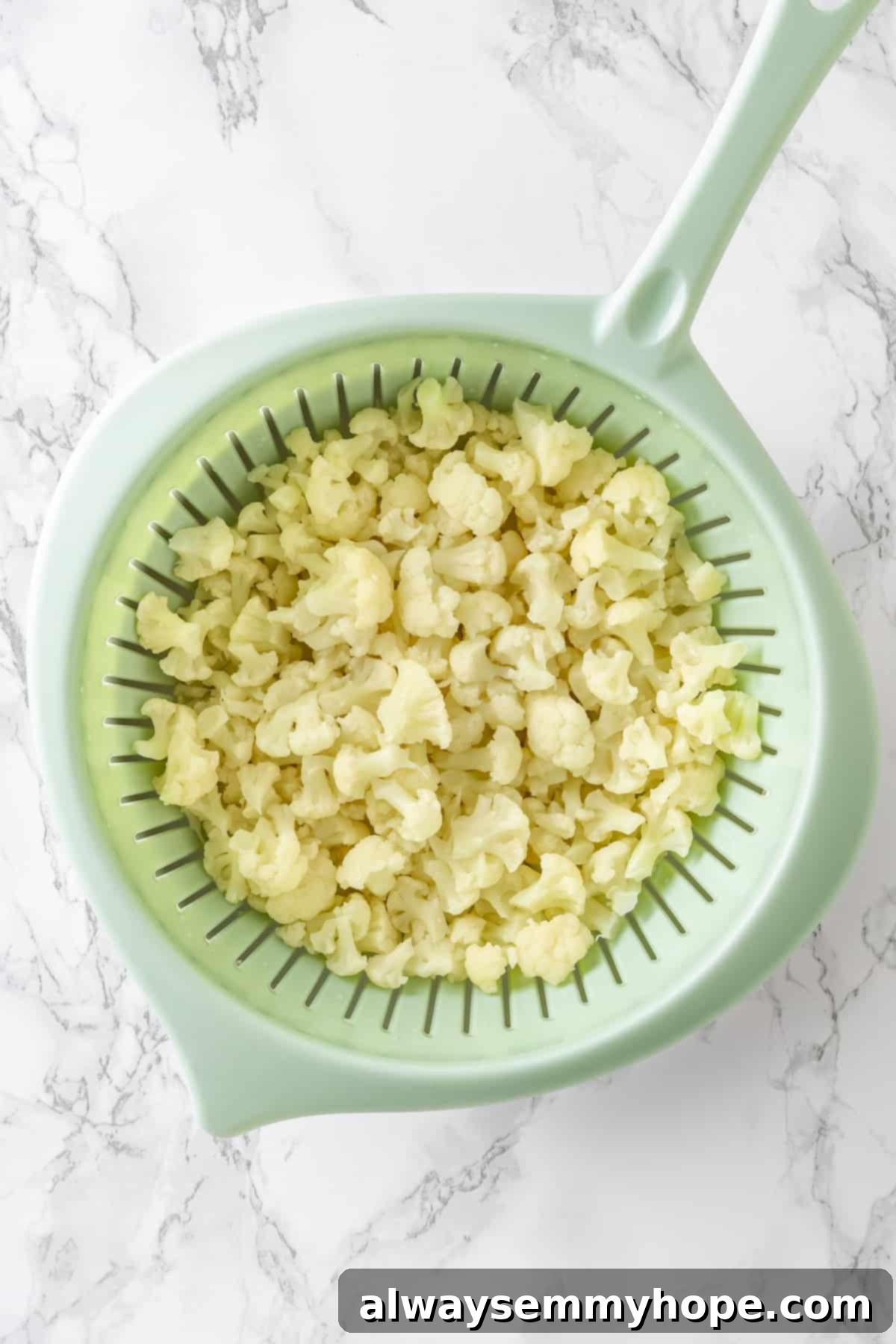 Overhead view of cooked cauliflower florets draining in a colander.